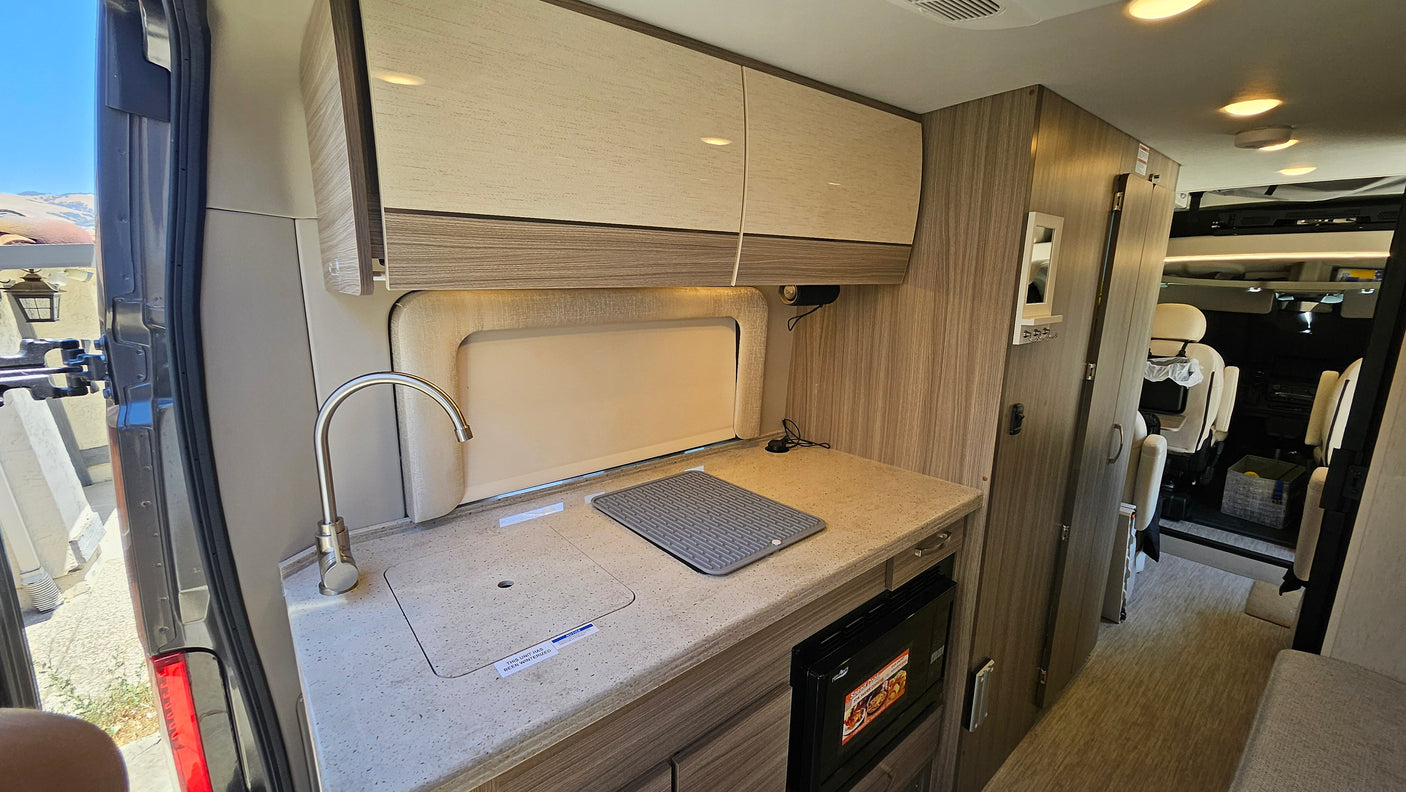 This rv rental features a well-equipped compact kitchen with a sink, microwave, overhead storage, and comfortable living space.