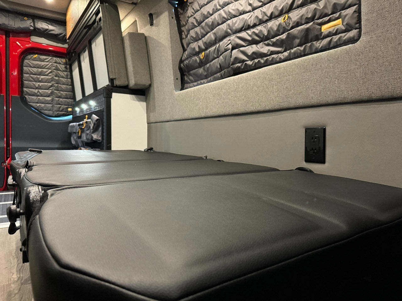 Explore this RV rental's cozy interior: modular black seating/bed, power outlet, insulated windows, ideal for mobile adventures.
