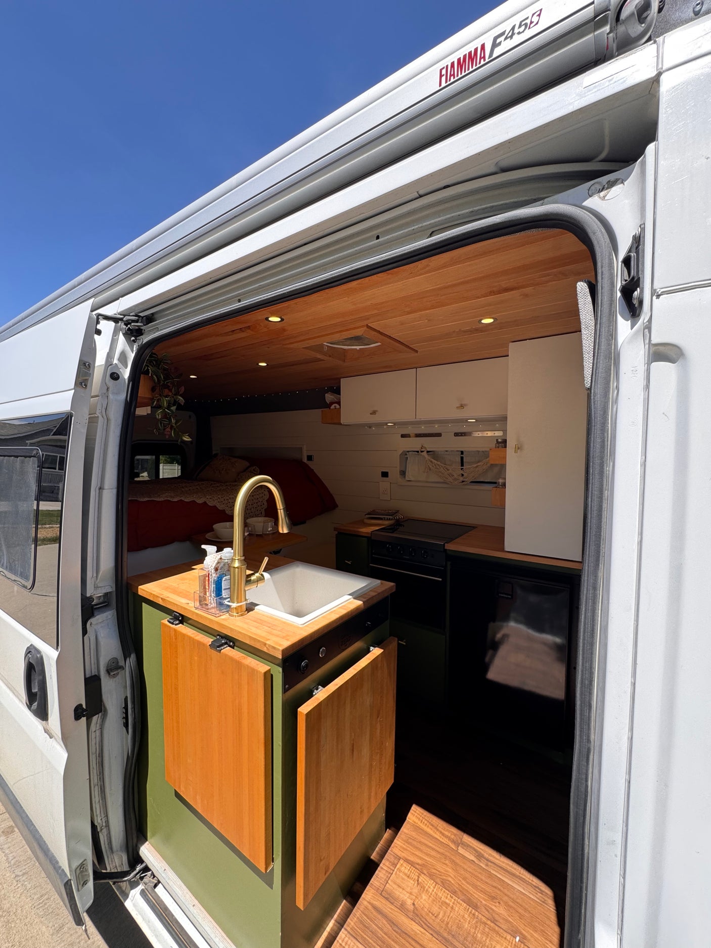 Open the door to this inviting rv rental camper van. View of a modern kitchen with sink, golden faucet, wooden ceiling, and bed.