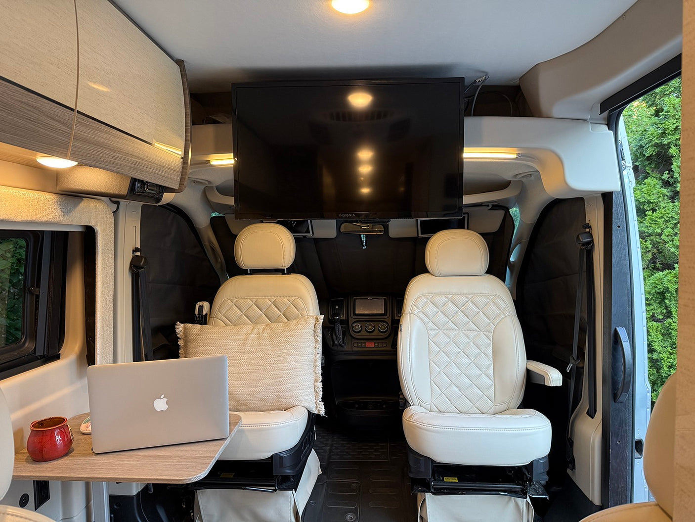 Modern RV rental interior with comfy cream seats, TV, and laptop workstation. Perfect for travel adventures.