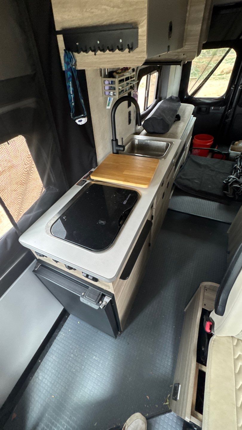 RV rental interior: A modern camper van kitchen with a sink, cooktop, fridge, and clever storage solutions.