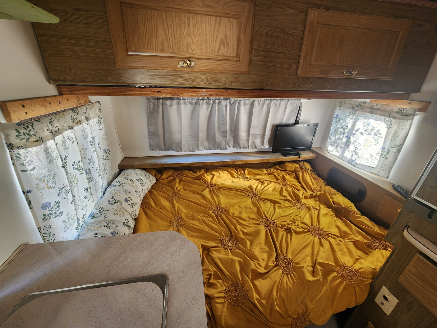 Inside an RV rental: a cozy bedroom with a vibrant yellow bed, floral curtains, and TV for a comfortable stay.