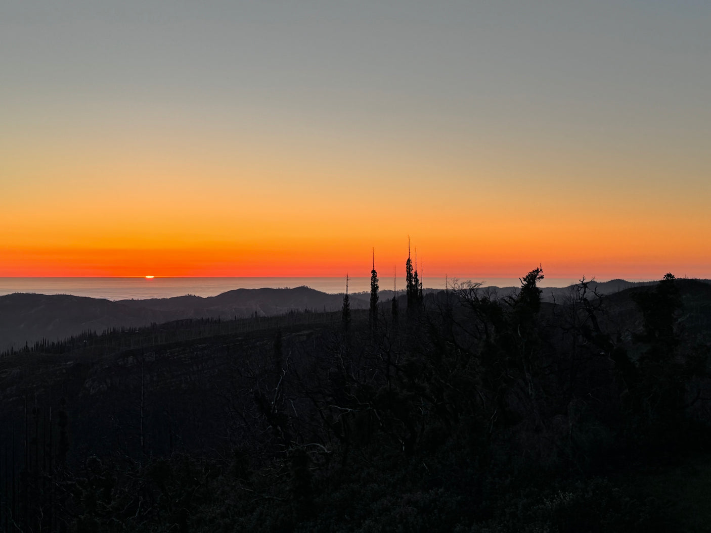 Golden sunset paints the sky above dark mountain silhouettes and distant fog. Explore these views with an RV rental!