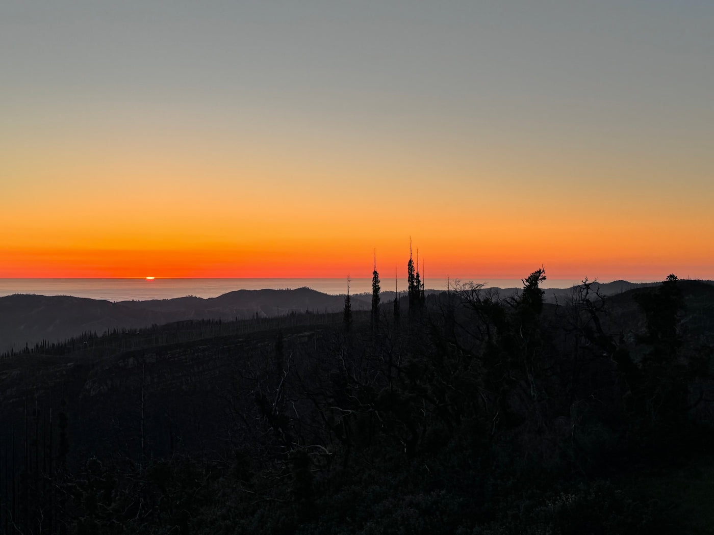 Golden sunset paints the sky above dark mountain silhouettes and distant fog. Explore these views with an RV rental! — photo 5