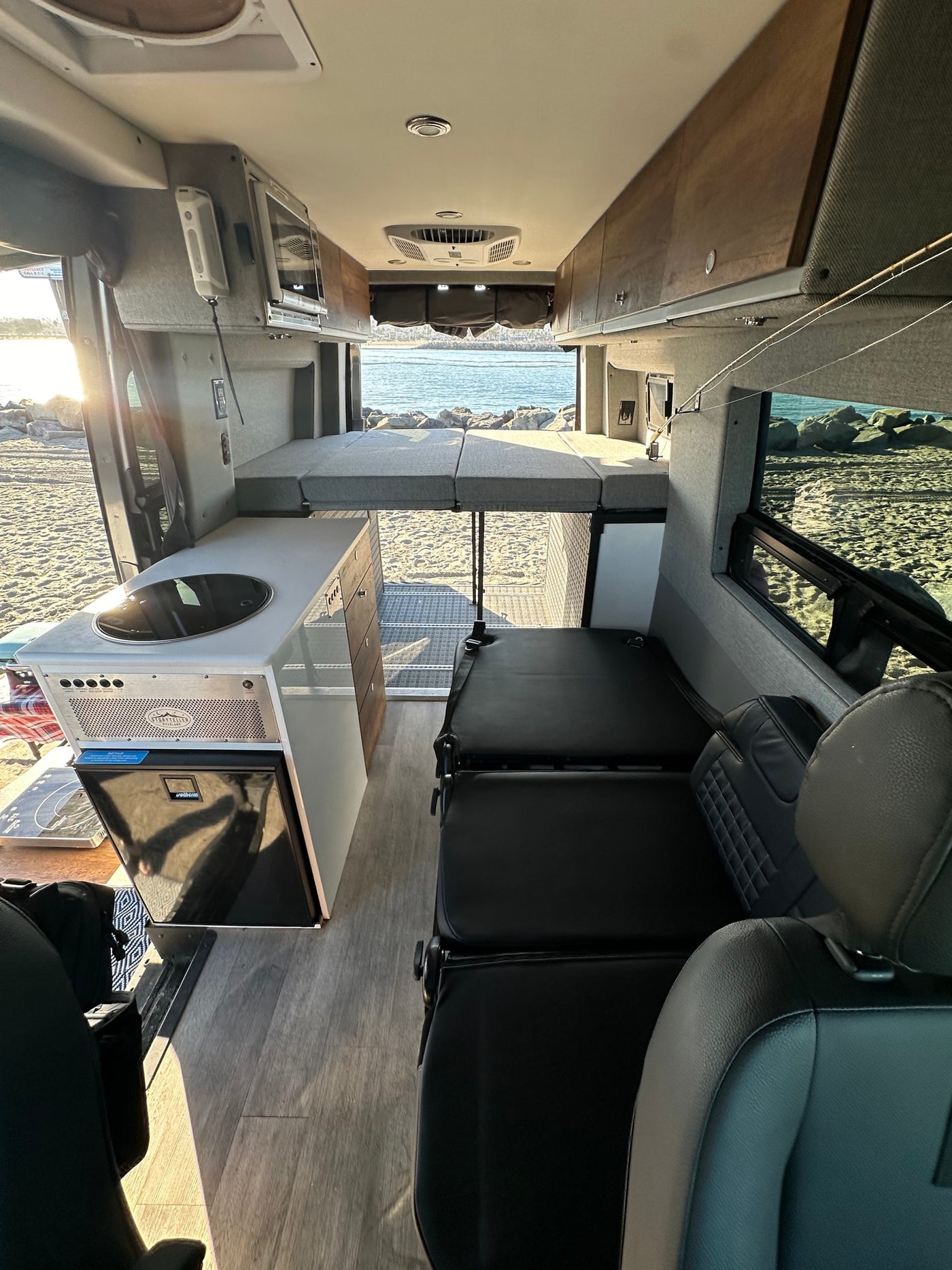 Coastal RV rental: spacious camper van interior with elevated bed, kitchenette, and beach/ocean view. — photo 8