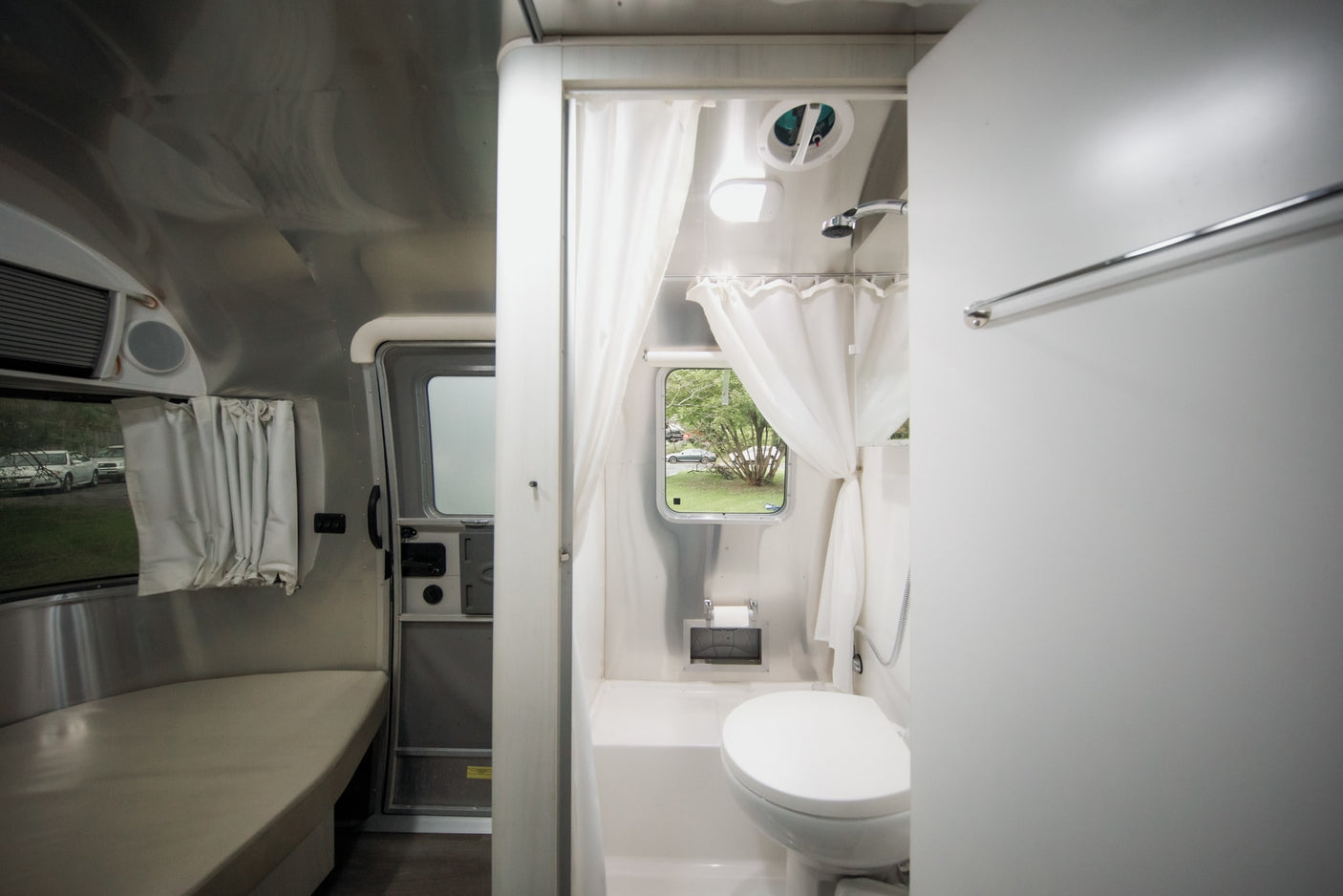 Inside a bright rv rental: compact bathroom with shower/toilet, adjacent to seating area and window views.