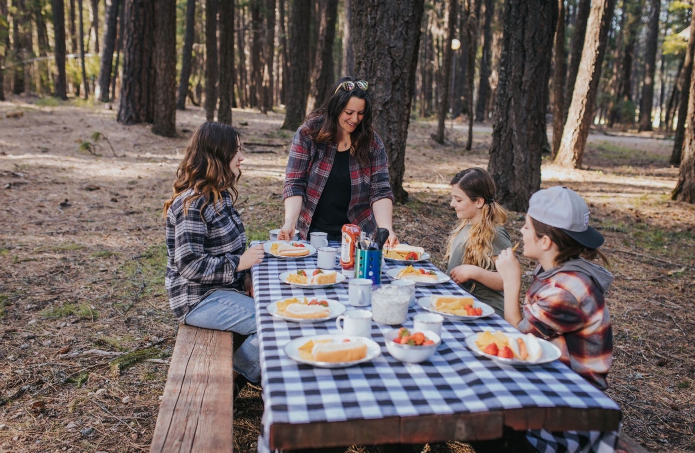 Four women share a picnic lunch at a checkered table in a wooded area, perfect for an RV rental adventure.