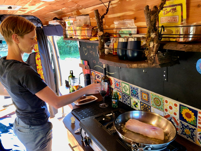 Person cooks fish in an RV rental kitchen, showing a cozy van life setup with custom details and meal prep.