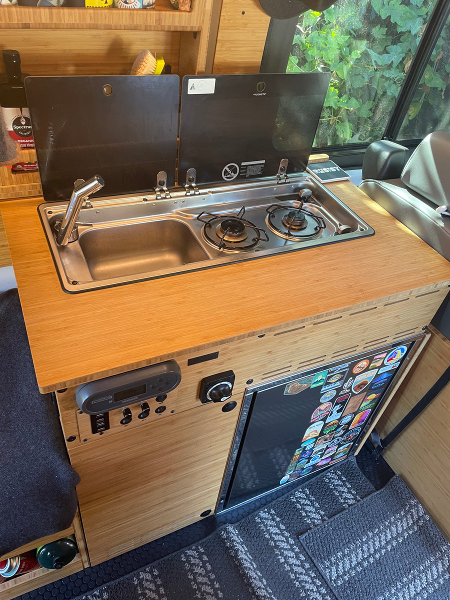 RV rental bamboo kitchen with integrated Dometic sink/stove, Redarc controls, and a refrigerator, ideal for travel.