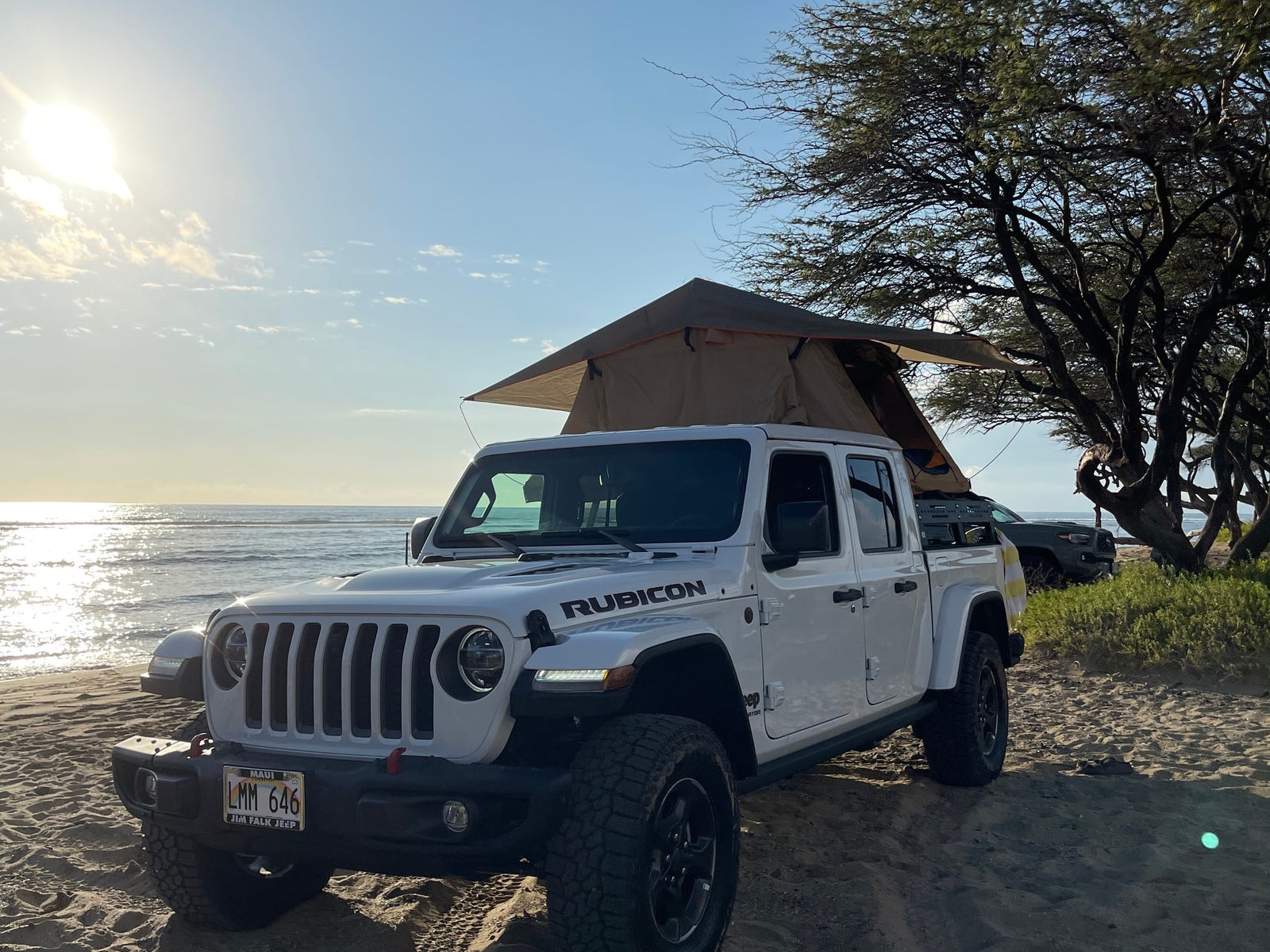 White Jeep Gladiator with rooftop tent on a sunny beach, ideal for a unique RV rental adventure.