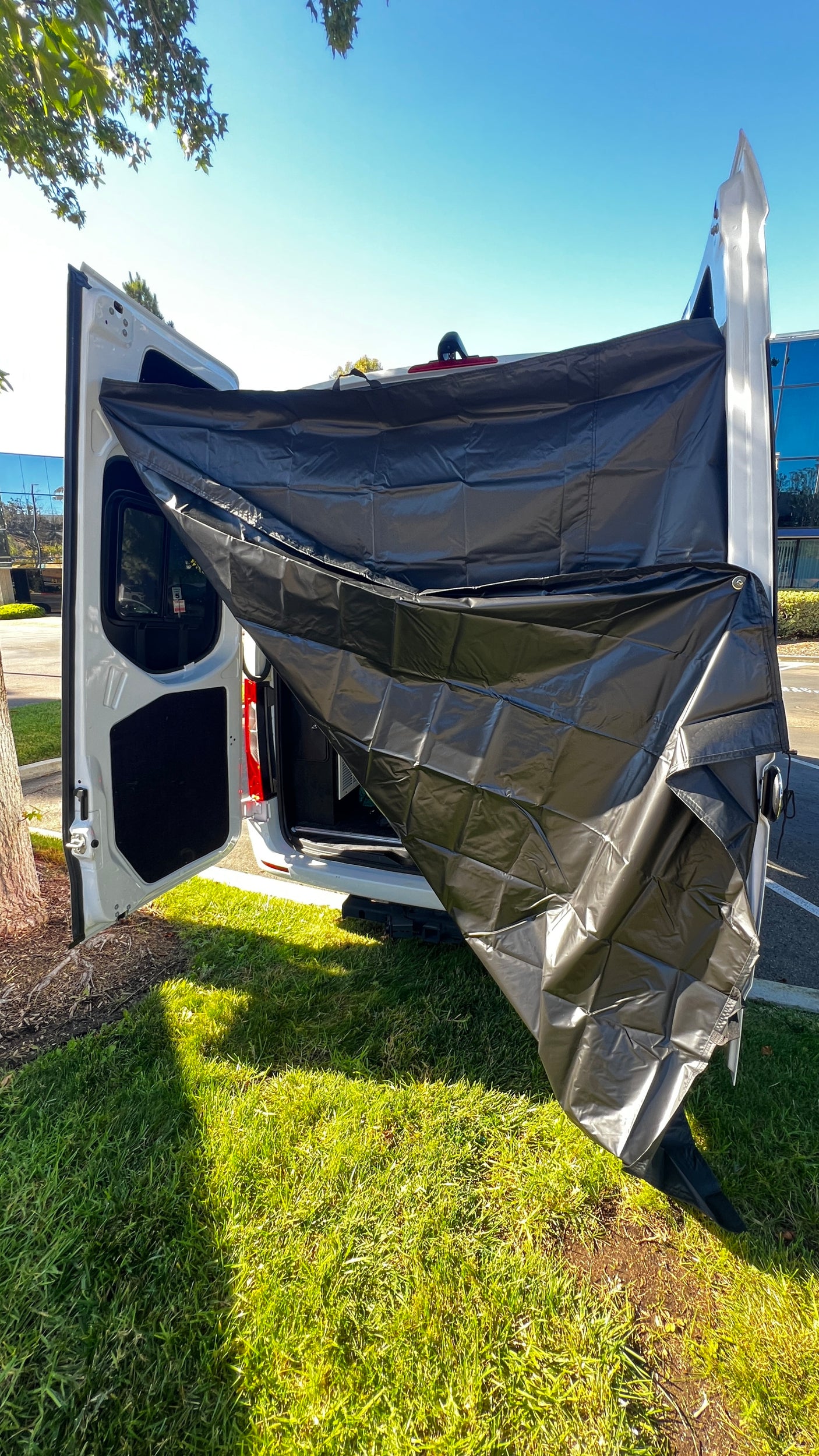 RV rental camper van with black privacy screen extended from open rear doors, parked on grass for outdoor use.