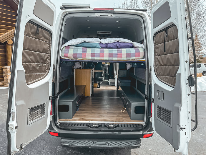 Open **RV rental** conversion van: reveals a cozy interior with a raised bed, storage benches, and wood flooring.