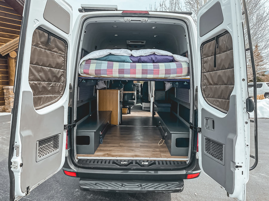 Open **RV rental** conversion van: reveals a cozy interior with a raised bed, storage benches, and wood flooring.
