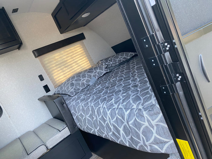 Cozy RV rental bedroom with a comfy patterned bed, window, and storage, perfect for your next road trip.