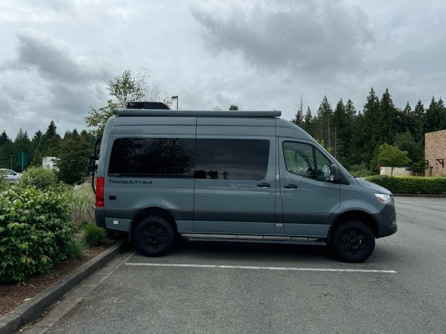parked amidst snow-covered pines under a clear blue sky.|Grey Mercedes Sprinter camper van — photo 2