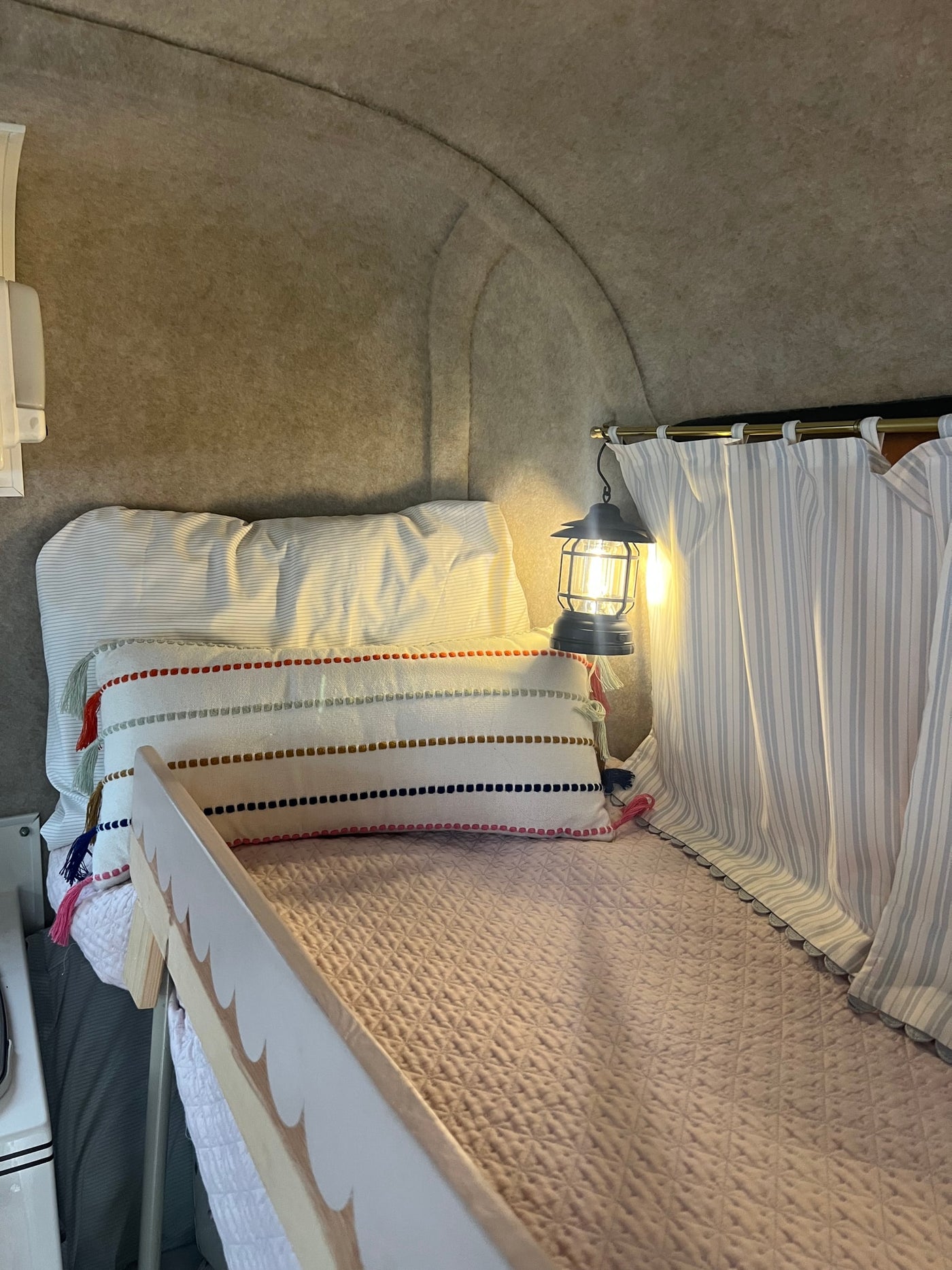 Cozy RV rental bunk bed with soft bedding, decorative pillow, warm lantern light, and striped curtains for a restful sleep. — photo 11