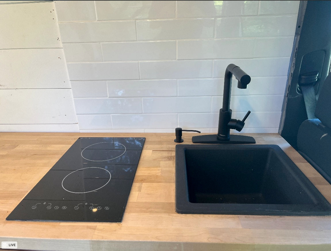 Modern RV rental kitchen with black induction cooktop, sink, faucet, and white subway tile backsplash.