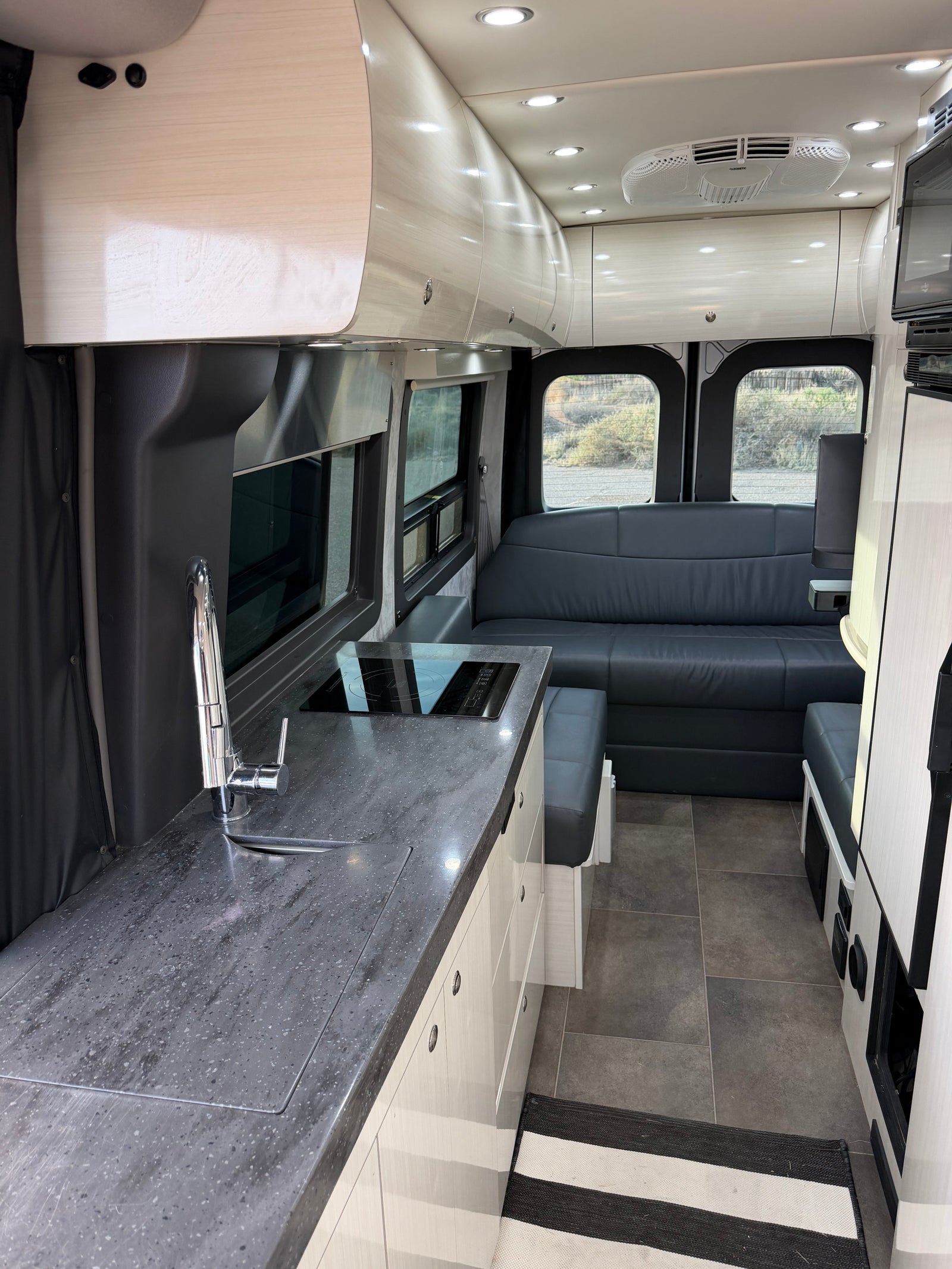 Spacious, modern RV rental interior with a sleek kitchen, comfy seating area, bright lighting, and an AC unit.