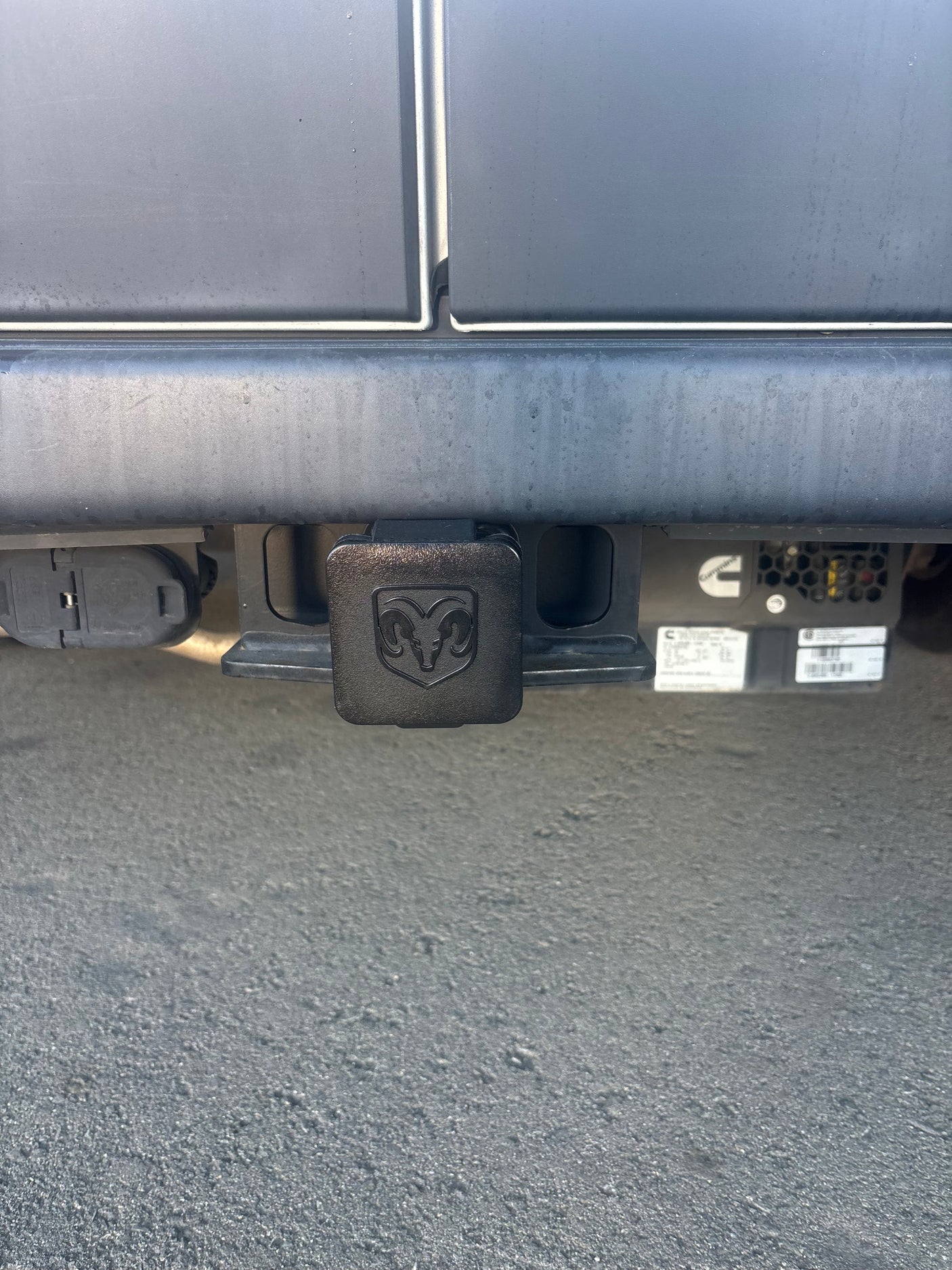 Rear view of an RV rental's trailer hitch with a Ram logo cover, trailer wiring connector, and a Cummins generator.