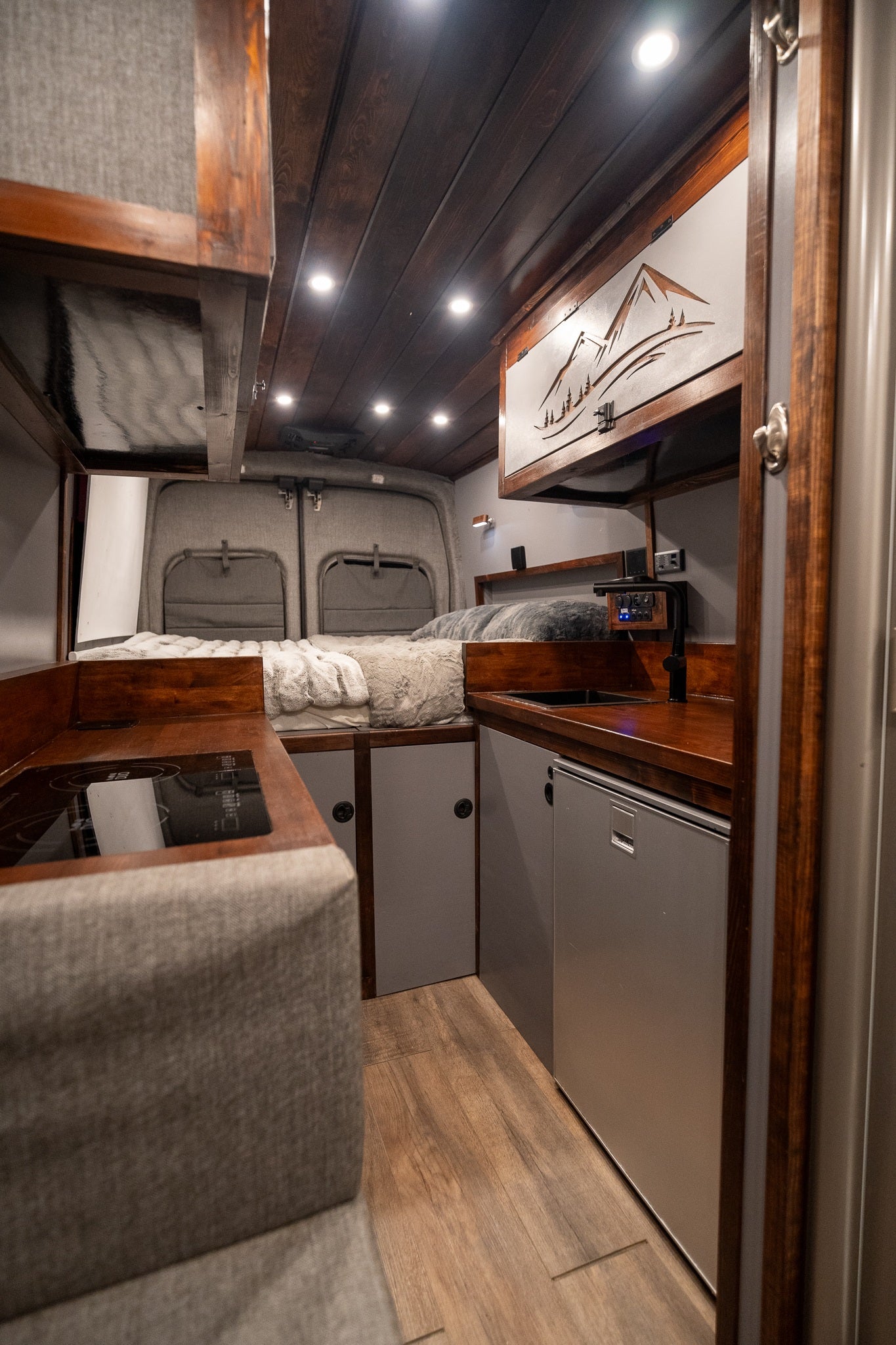 Cozy camper van interior featuring bed, kitchen, and wood accents, perfect for your next RV rental adventure.