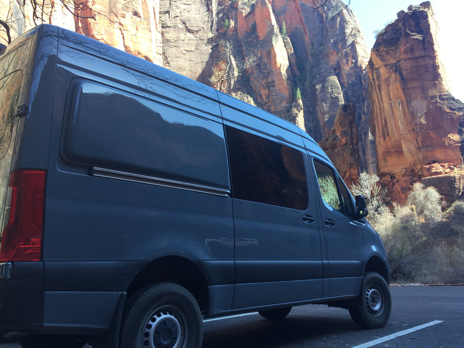 Dark gray RV rental van parked by towering red rock canyon walls. Perfect for a national park adventure.