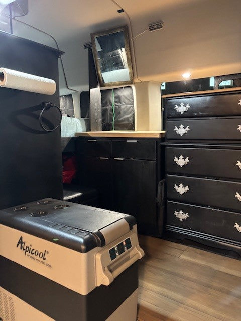 Inside this RV rental: Alpicool portable freezer, custom black cabinetry, and a dresser with decorative pulls, offering storage.