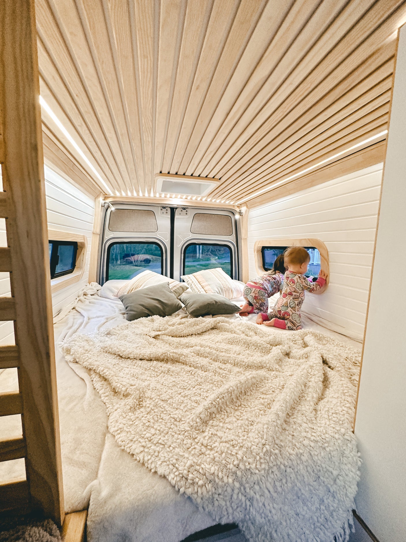 Cozy RV rental interior with two toddlers exploring the comfy bed and custom wood-paneled walls. Perfect for family travel.