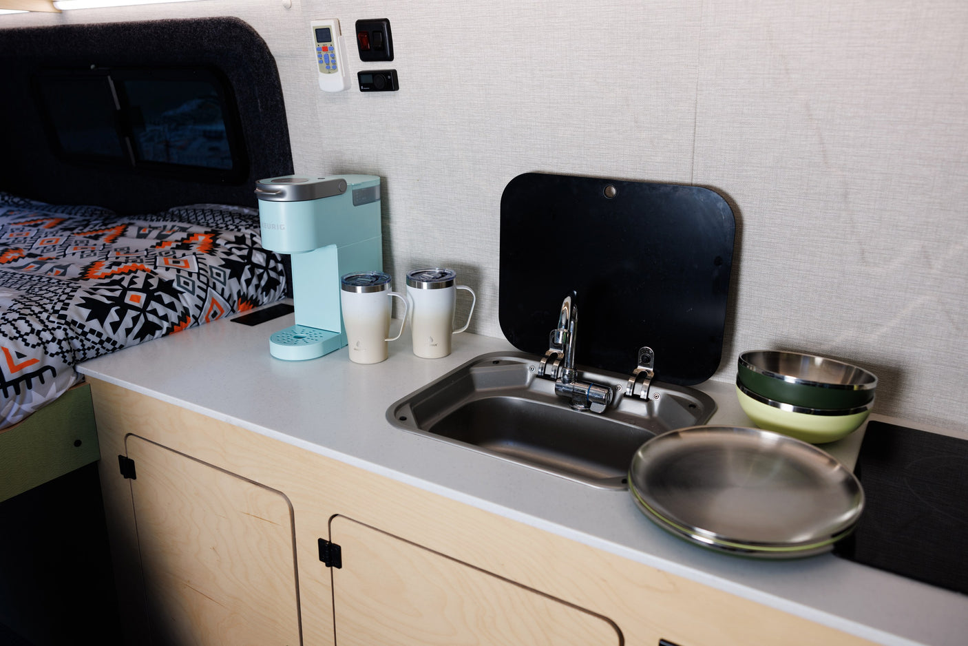 This RV rental features a cozy kitchenette with a Keurig coffee maker, sink, dishes, and an adjacent bed area.