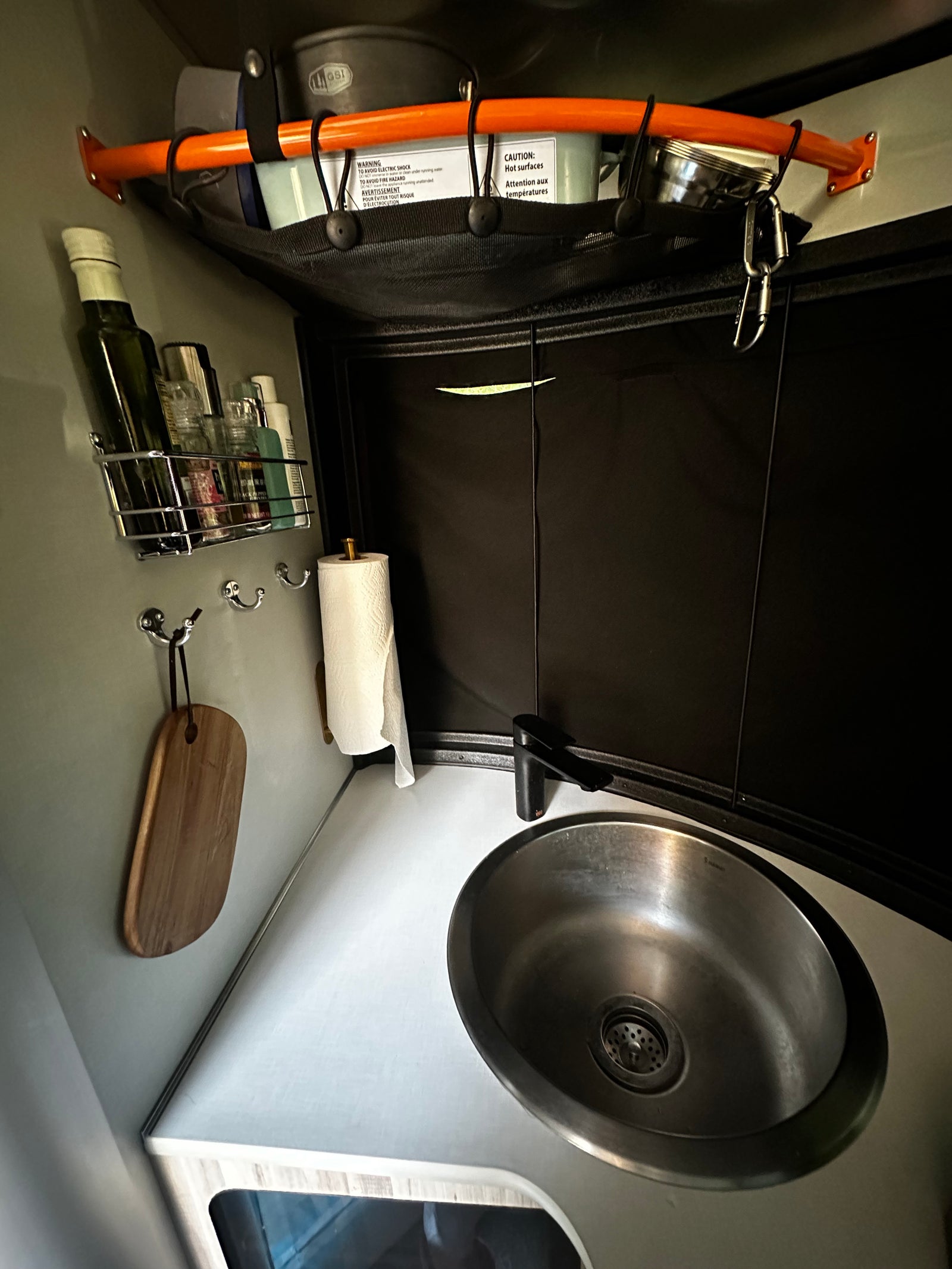 RV rental compact kitchen with sink, overhead mesh storage for cookware, & wall-mounted spice rack. Ideal for travel.