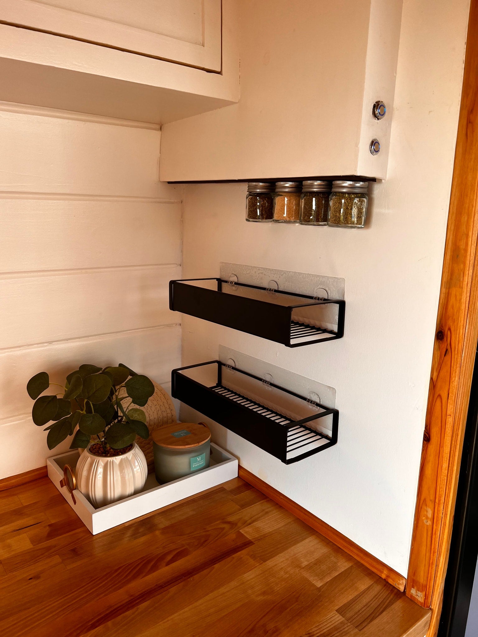 Smart RV rental kitchen. Magnetic spice jars & wall shelves optimize storage. Countertop features a plant & candle.