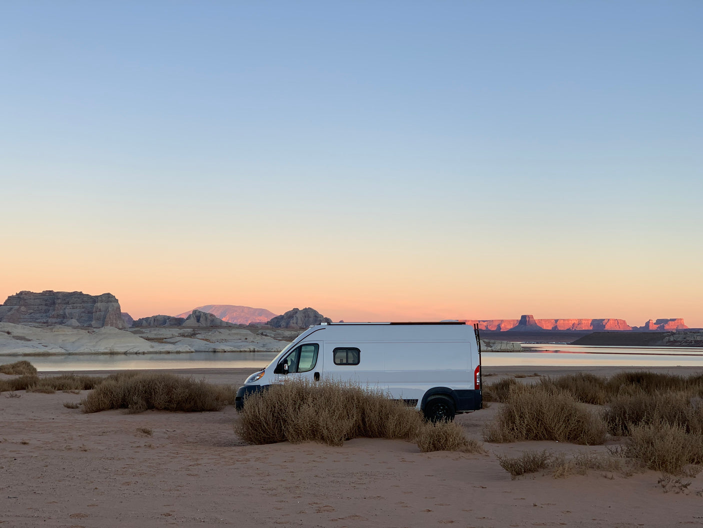 RV rental parked by a serene desert lake at sunrise or sunset, showcasing the beauty of rock formations.