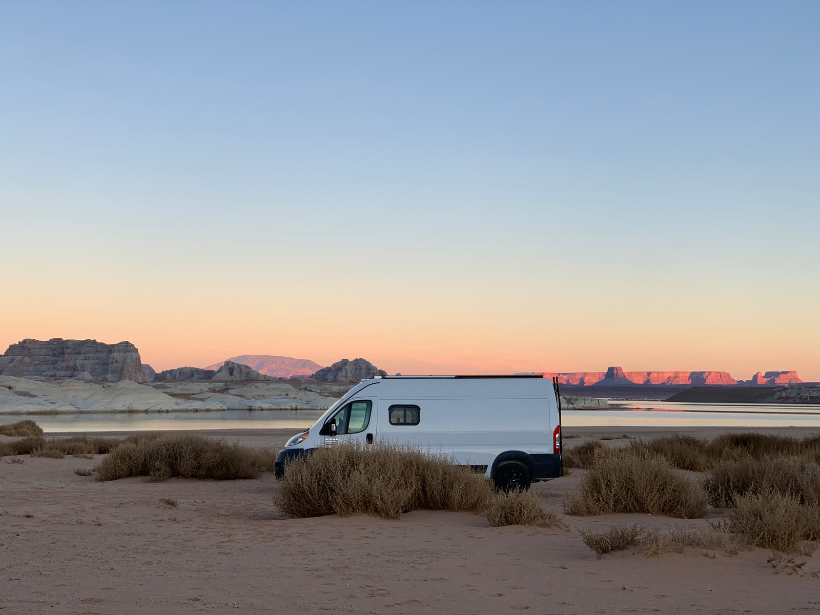 RV rental parked by a serene desert lake at sunrise or sunset, showcasing the beauty of rock formations.