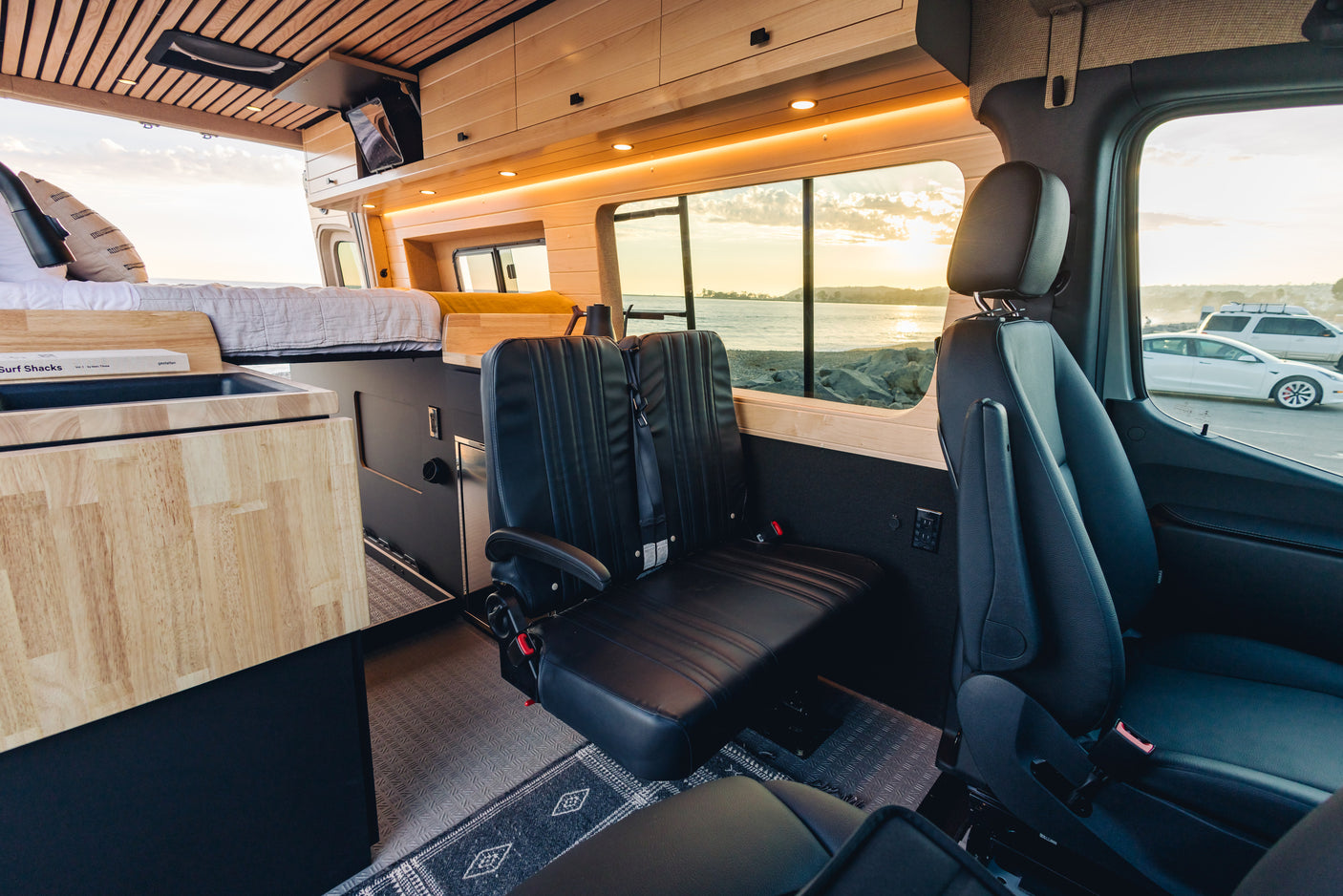 Spacious, wood-paneled RV rental interior with bed, seating, and stunning sunset ocean views from your camper van.
