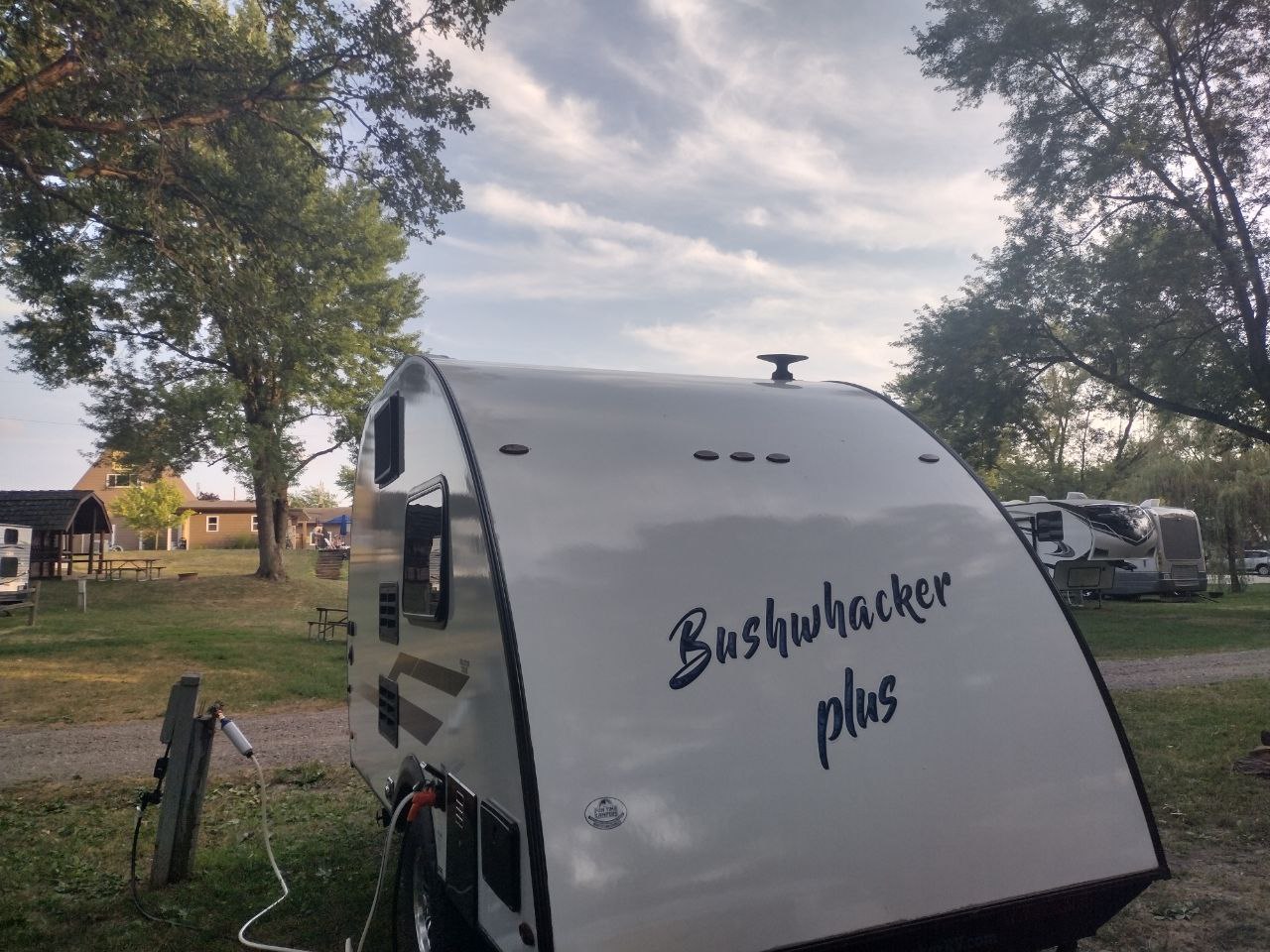 parked on grass at a shady campsite. Ideal for outdoor adventures.|Bushwhacker Plus travel trailer RV rental