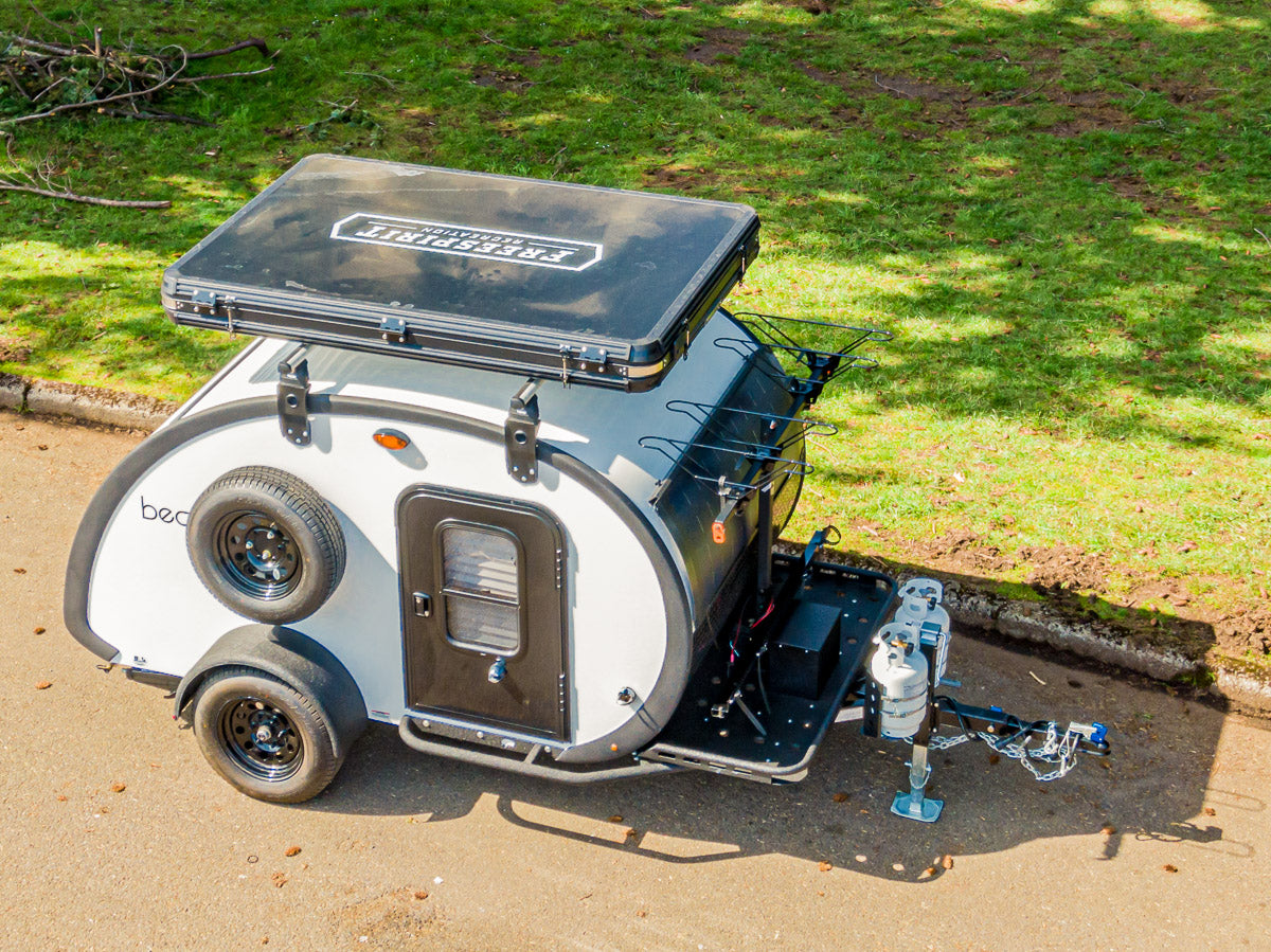 This compact white & black teardrop camper, ideal for rv rental, features a rooftop tent & propane tanks.