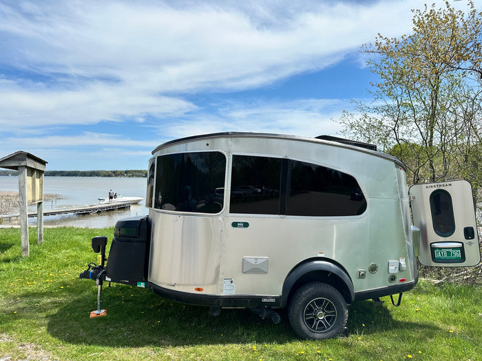 A sleek Airstream rv rental parked on grassy lake shore, with a boat on the water & trees. Perfect for scenic camping.
