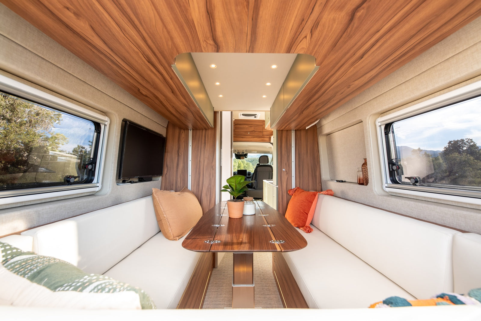 Spacious RV rental interior with wooden ceiling, white bench seating, and dining table. Enjoy scenic views from this comfortable camper.