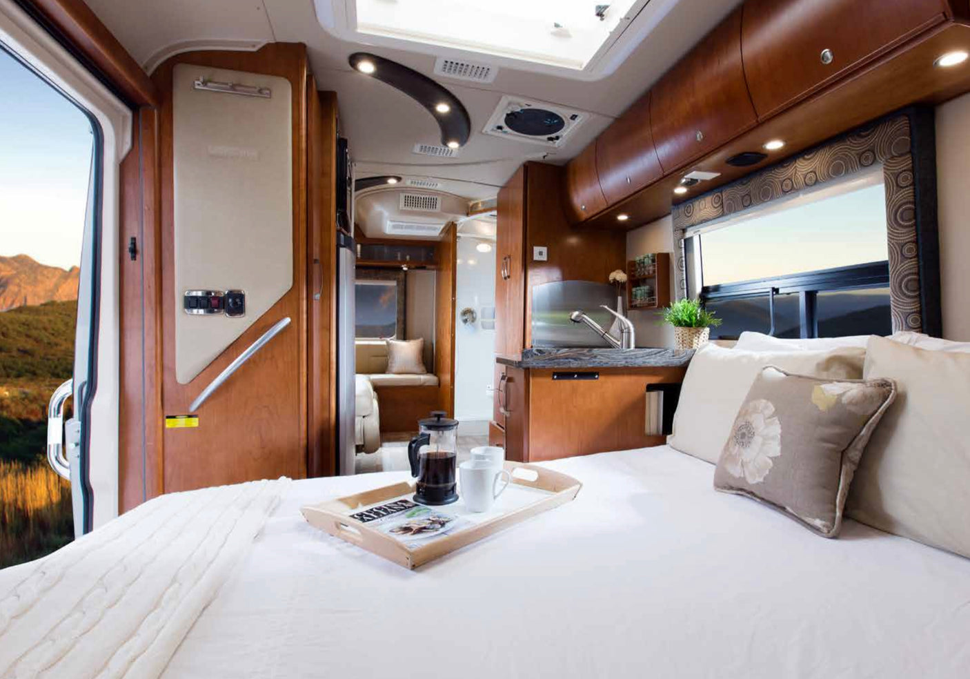 Luxurious RV rental interior featuring a spacious bed, kitchen area, and mountain views outside.