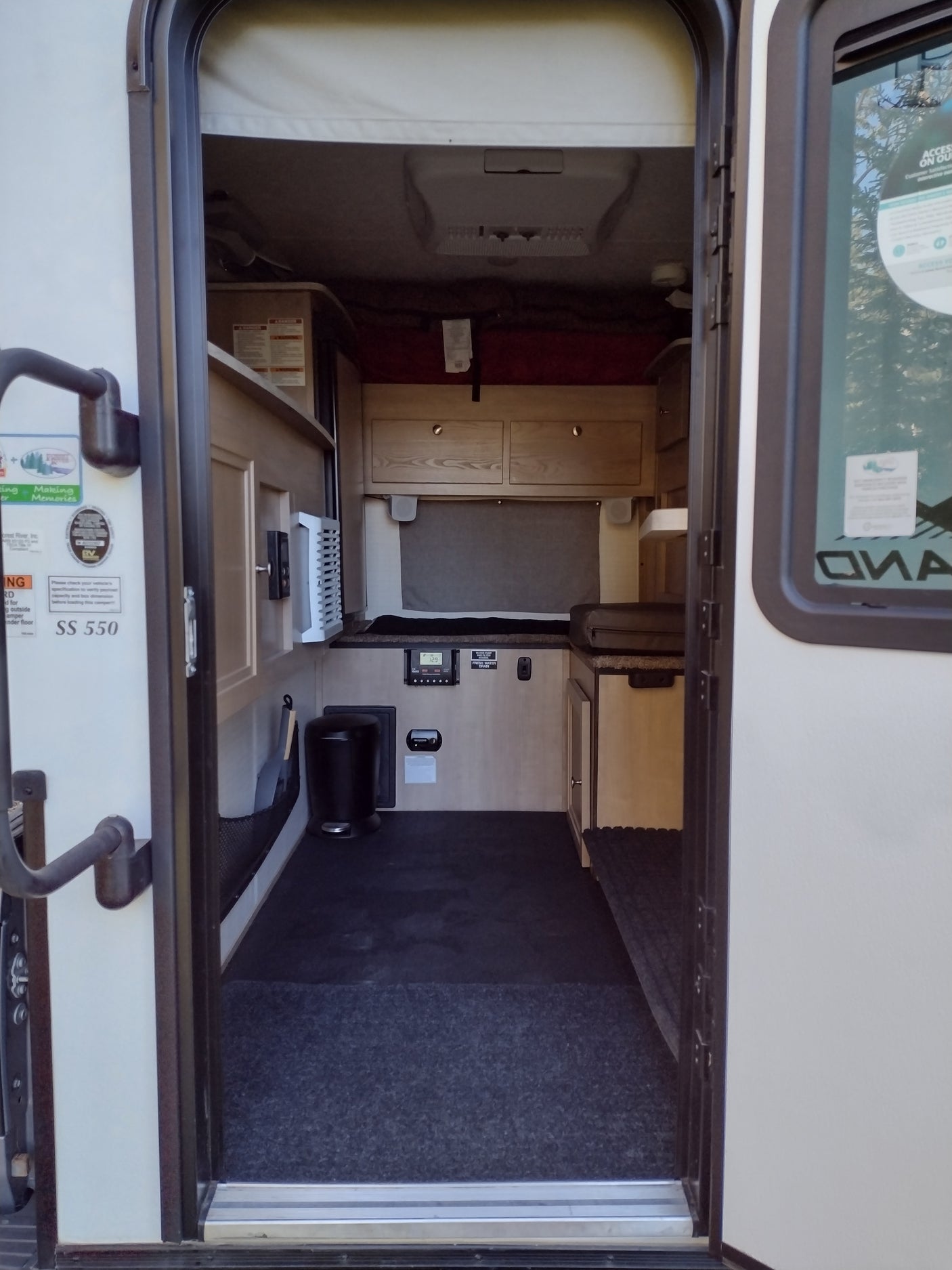 Interior view of an RV rental, showing a bed, overhead AC, storage cabinets, and control panel for easy living on the road.