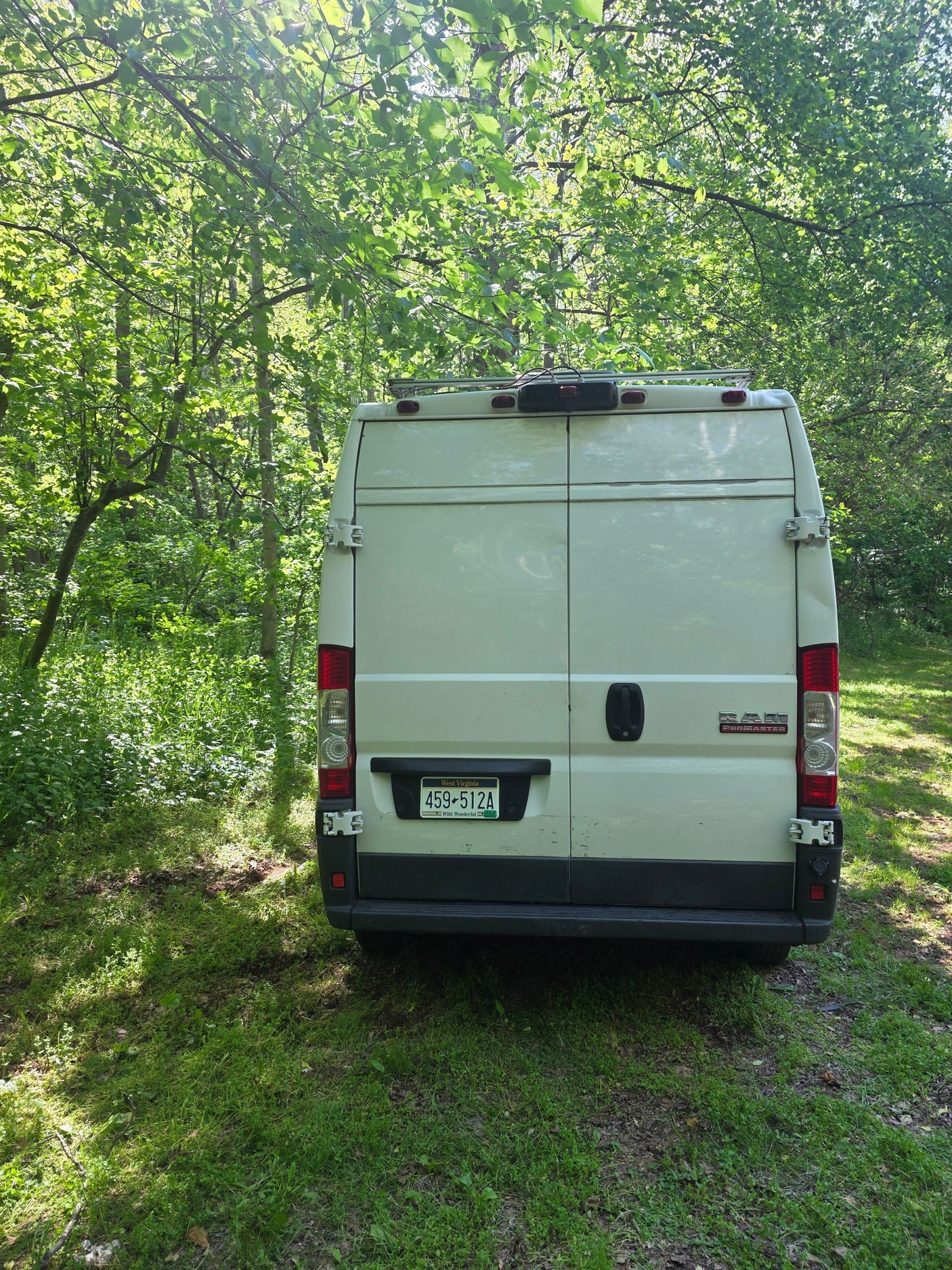 White Ram ProMaster van (rv rental) parked in a sun-dappled forest, showing its rear with a West Virginia license plate.