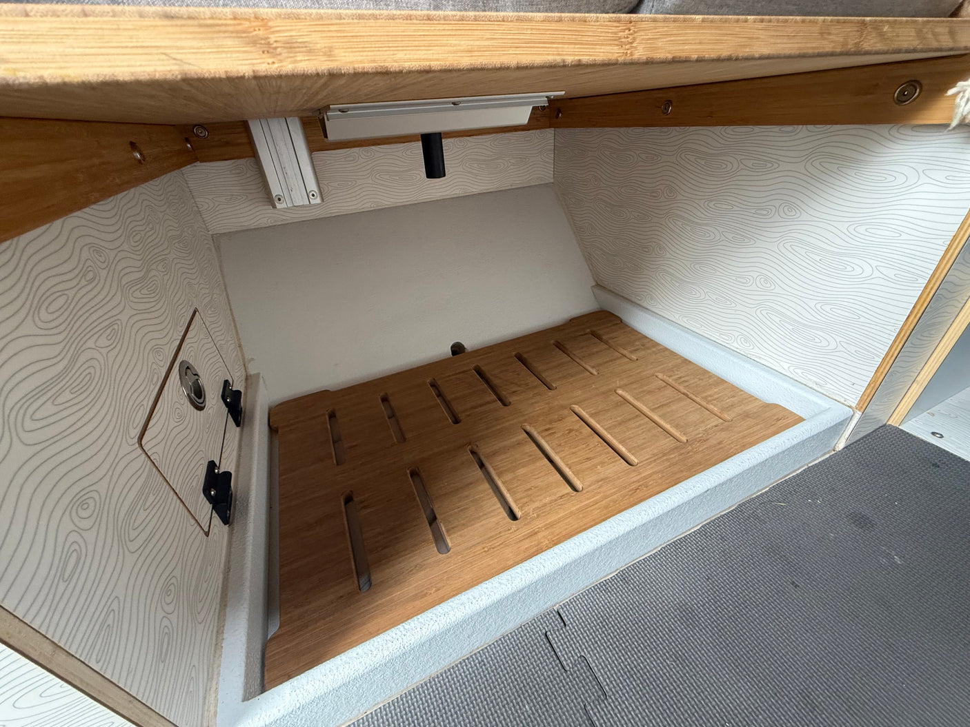 RV rental wet bath with bamboo slatted floor, topographic wall pattern, and shower head. Compact, functional camper shower.
