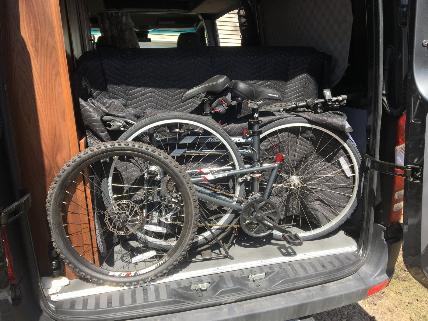 Two folding bicycles stored in an RV rental van's rear, on a protective quilted blanket.