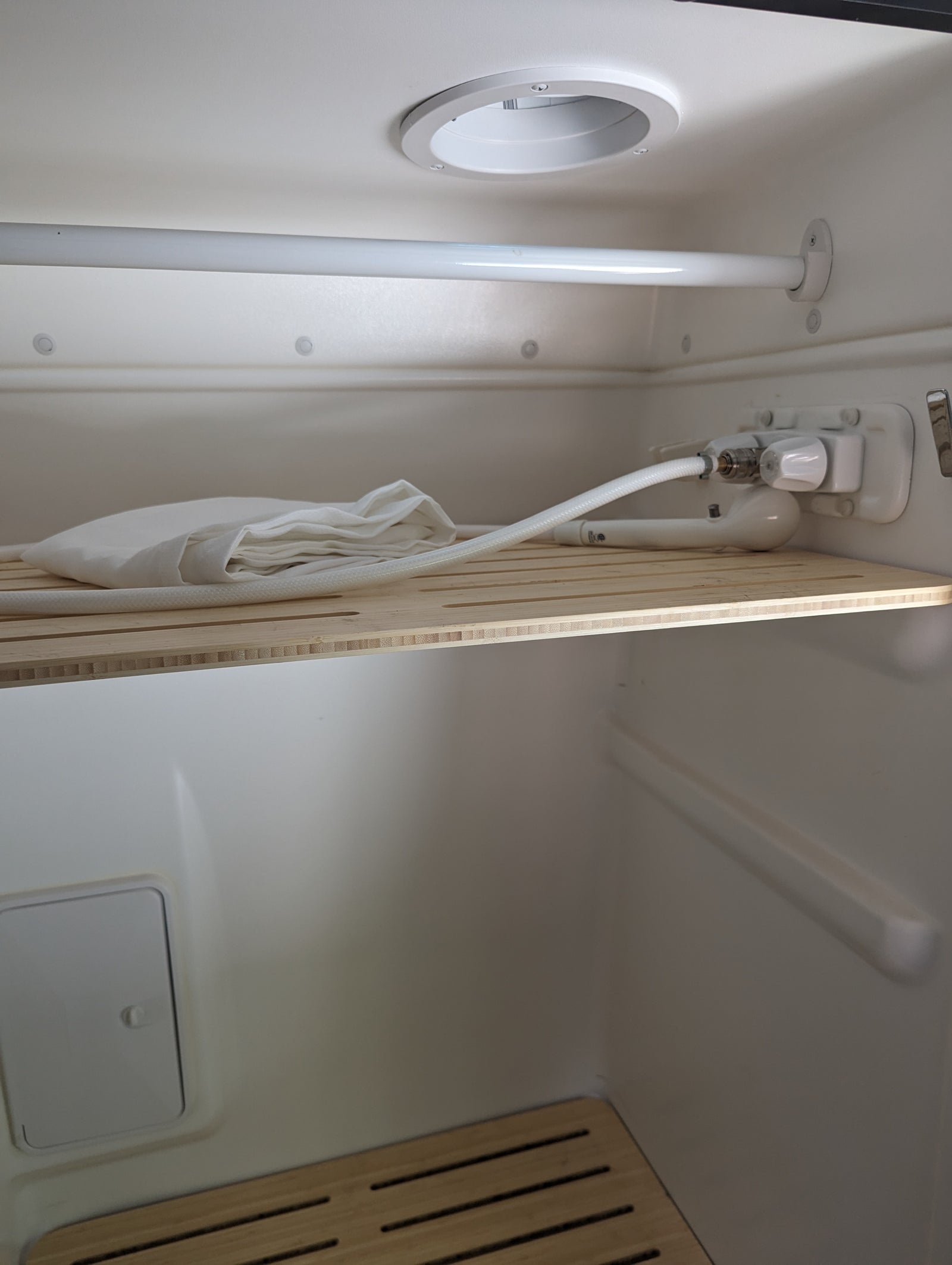 rv rental compact wet bath interior, showing shower controls, hose, white towel, and slatted wooden shelf.