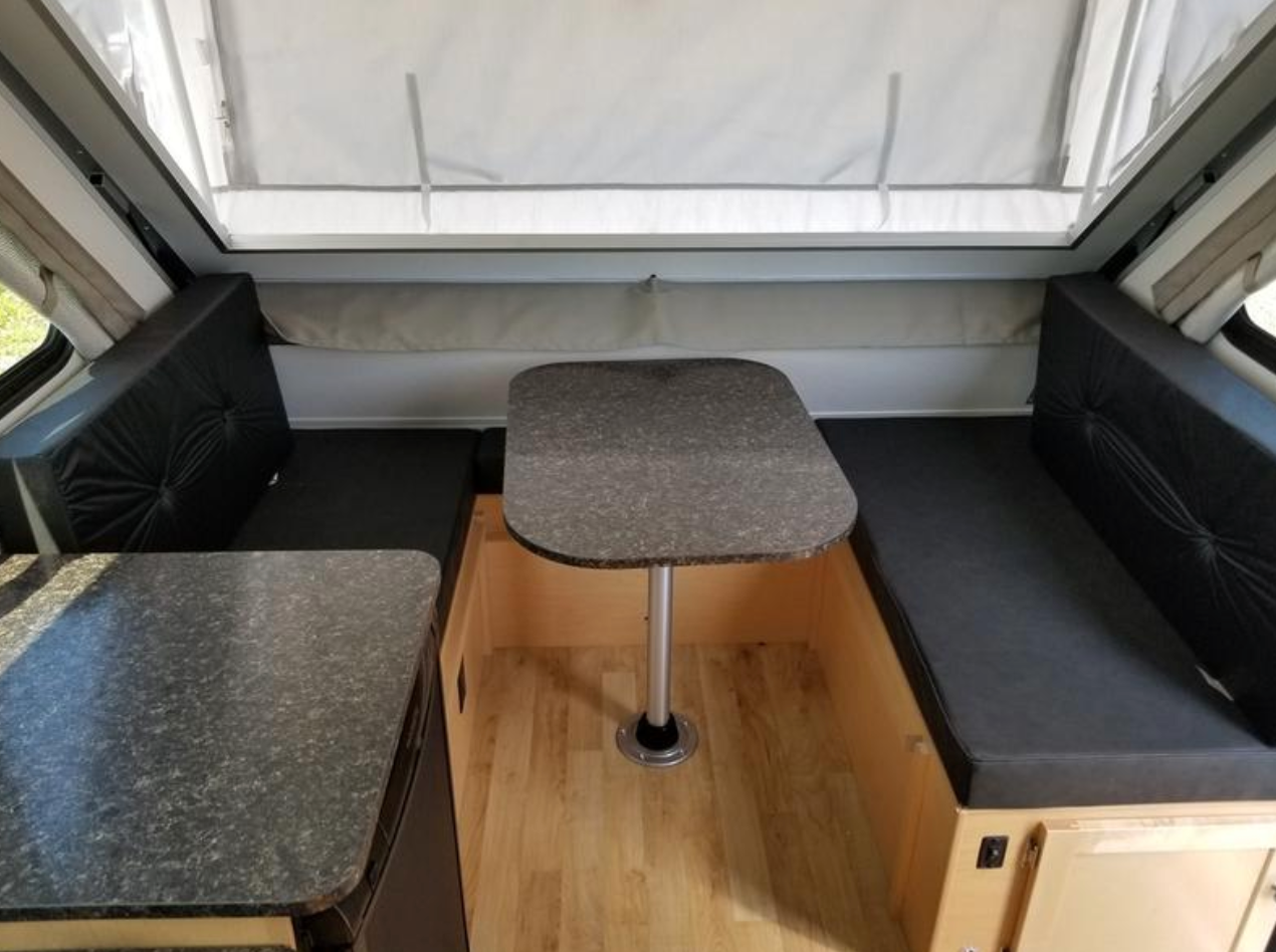 Experience comfort in this RV rental's dinette, featuring black cushioned benches, a table, and wood interior.