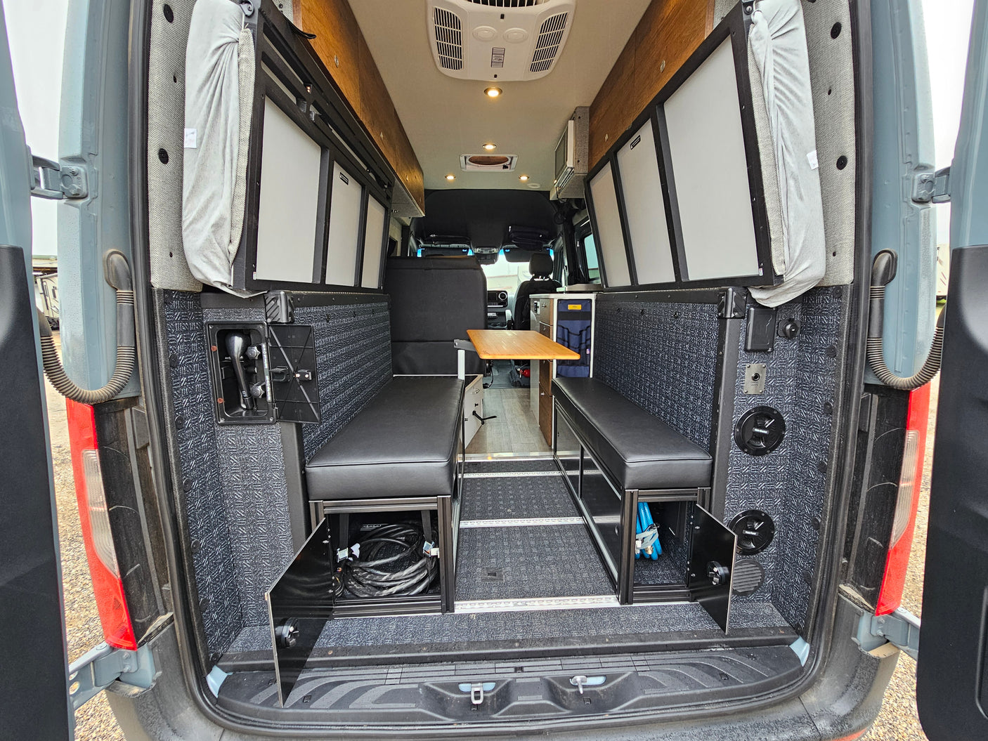 Step into this spacious RV rental camper van interior, featuring rear-facing bench seating, a dining table, overhead cabinets, and practical storage.