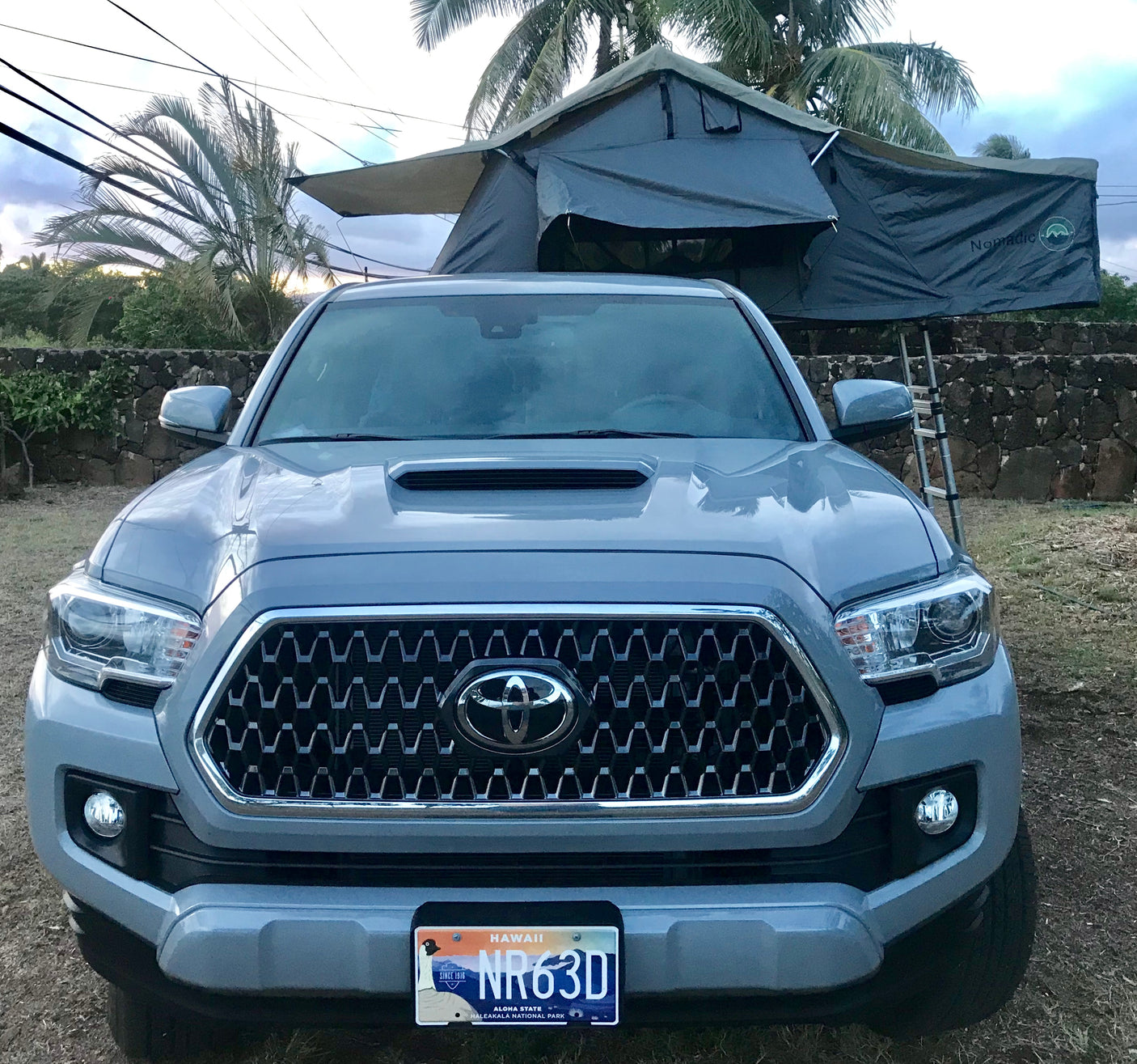 Front of a grey Toyota Tacoma pickup truck, equipped with a Nomadic rooftop tent, ideal as an RV rental in Hawaii.
