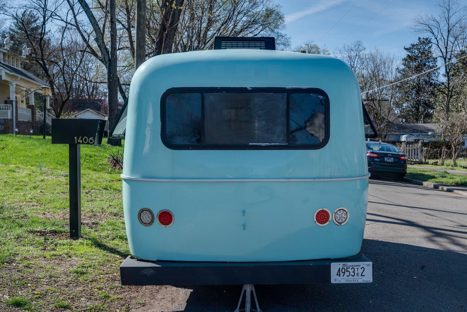 Rear view of a light blue RV rental, a Tennessee travel trailer (4953T2) parked in a residential area by mailbox 1406.