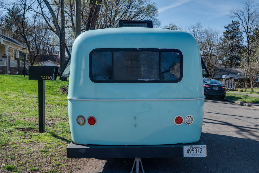 Rear view of a light blue RV rental, a Tennessee travel trailer (4953T2) parked in a residential area by mailbox 1406.