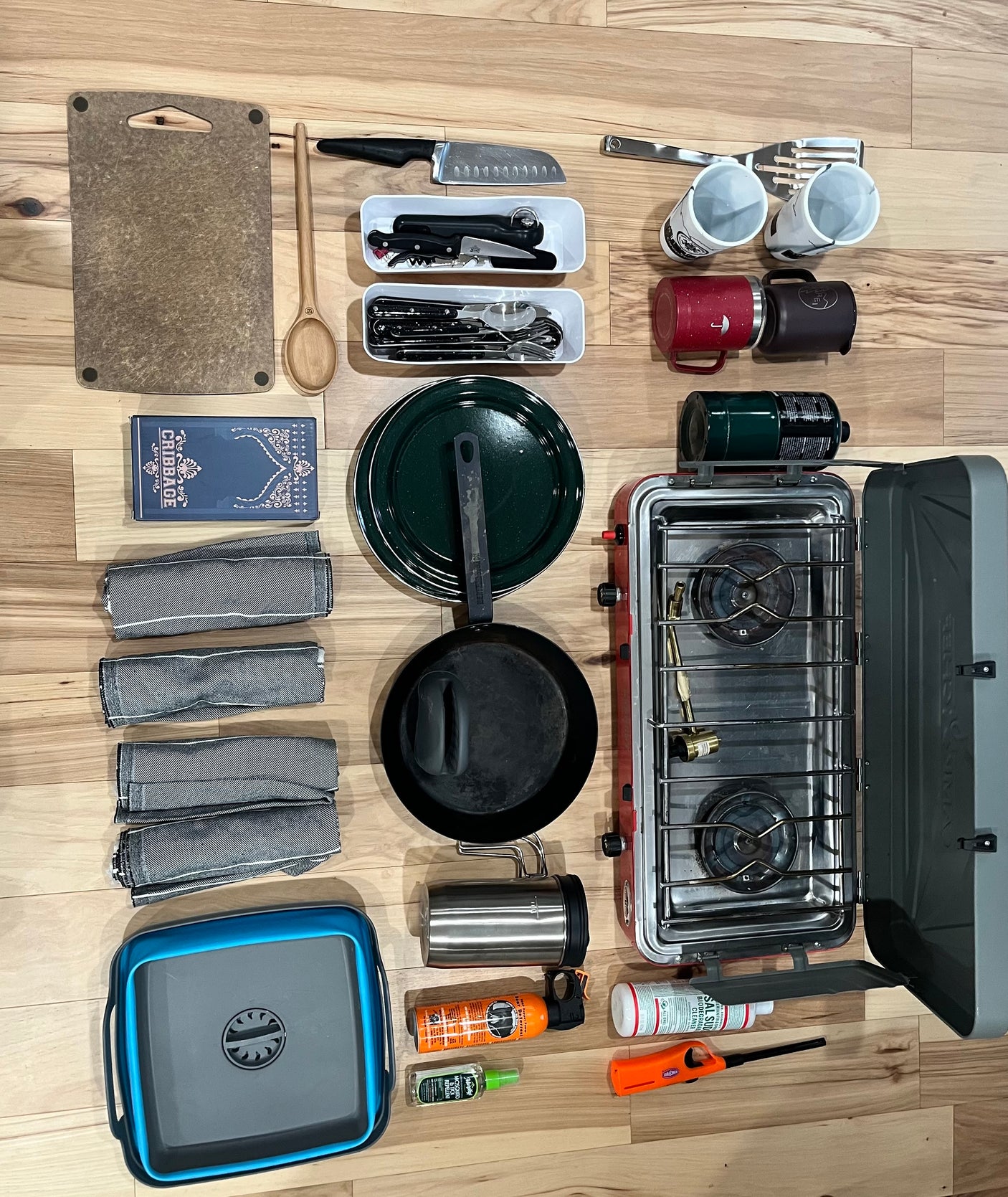 Prepped for an RV rental adventure! Camping kitchen essentials: stove, pans, cutlery, mugs, towels, and safety items laid out.