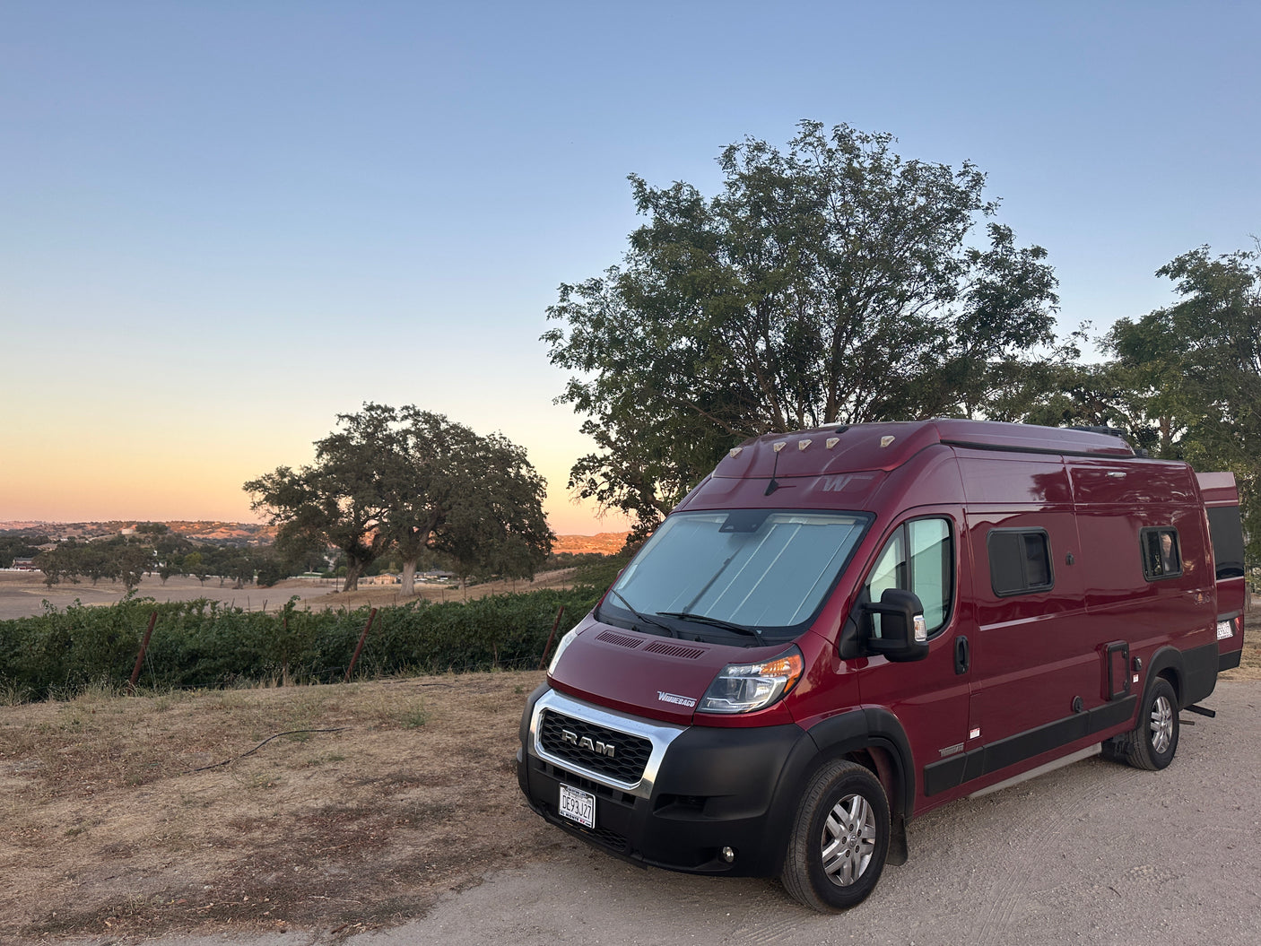 Red Winnebago Solis camper van rv rental at sunset, parked near a vineyard. Ideal for a scenic road trip.